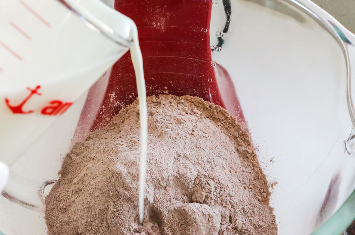 Pouring milk into a mixer filled with chocolate cake mix.