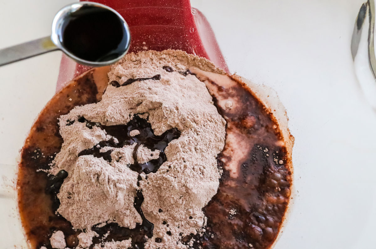 Adding a teaspoon of vanilla extract to the mixing bowl filled with chocolate cake mix.