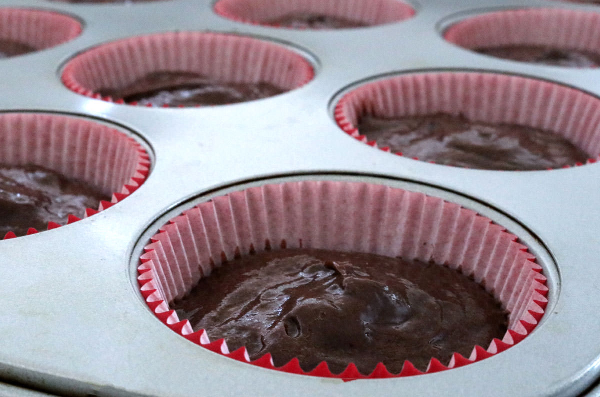 A cupcake pan filled with red cupcake  liners and chocolate cake batter.