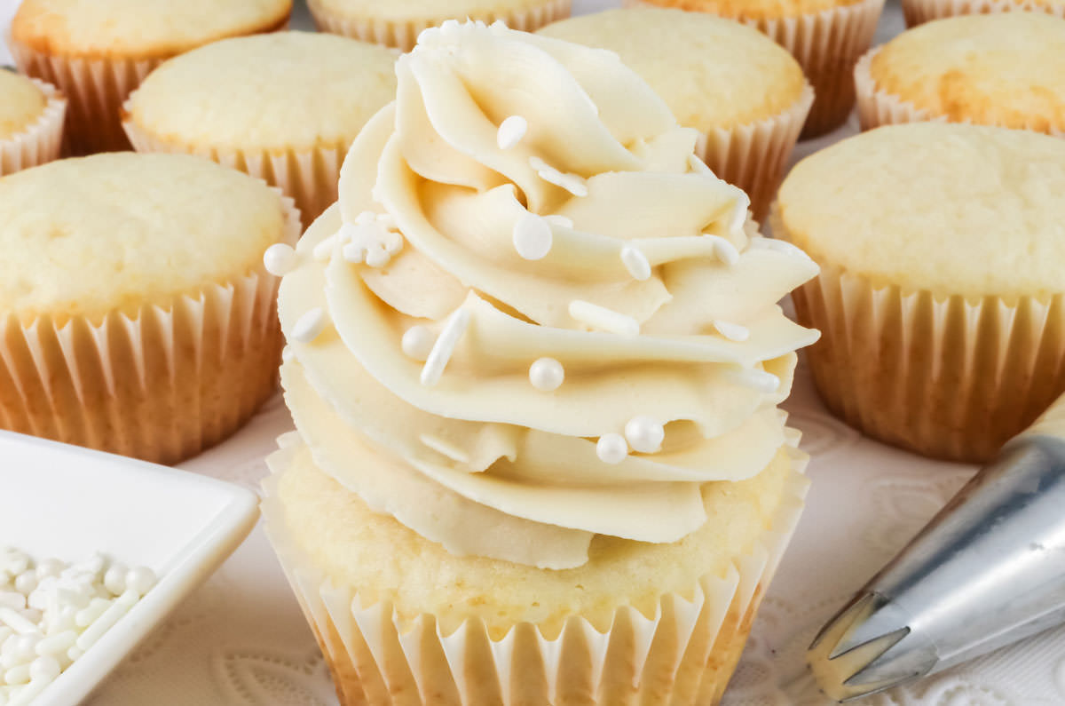 Closeup on a white cupcake with a white cupcake liner frosted with homemade buttercream frosting.