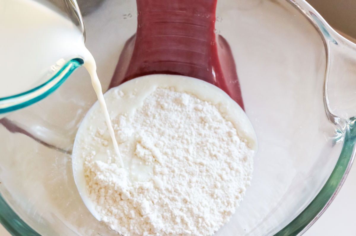 Pouring milk into a mixing bowl filled with white cake mix.