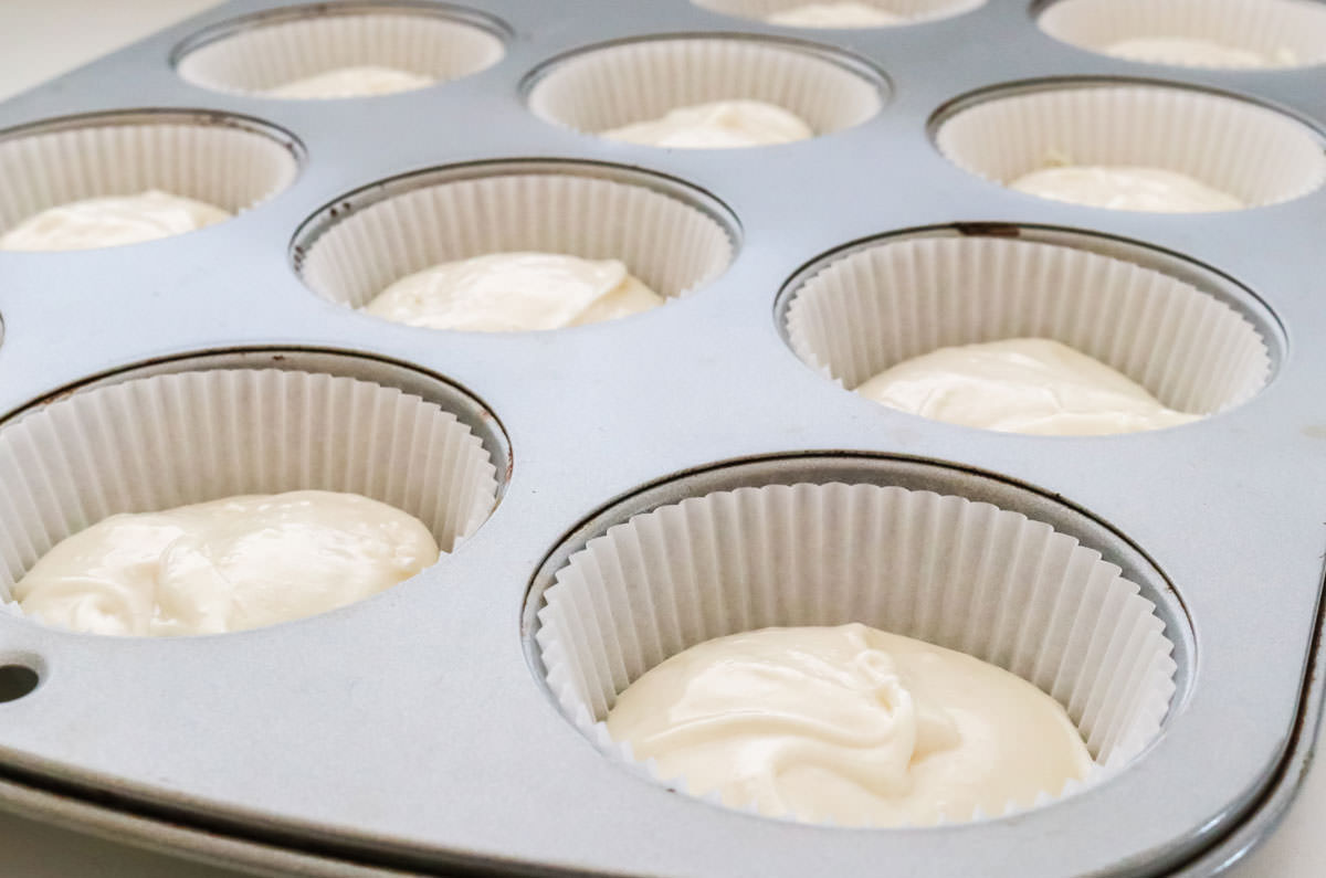 Closeup on a cupcake pan filled with white cupcake liners and white cake batter.